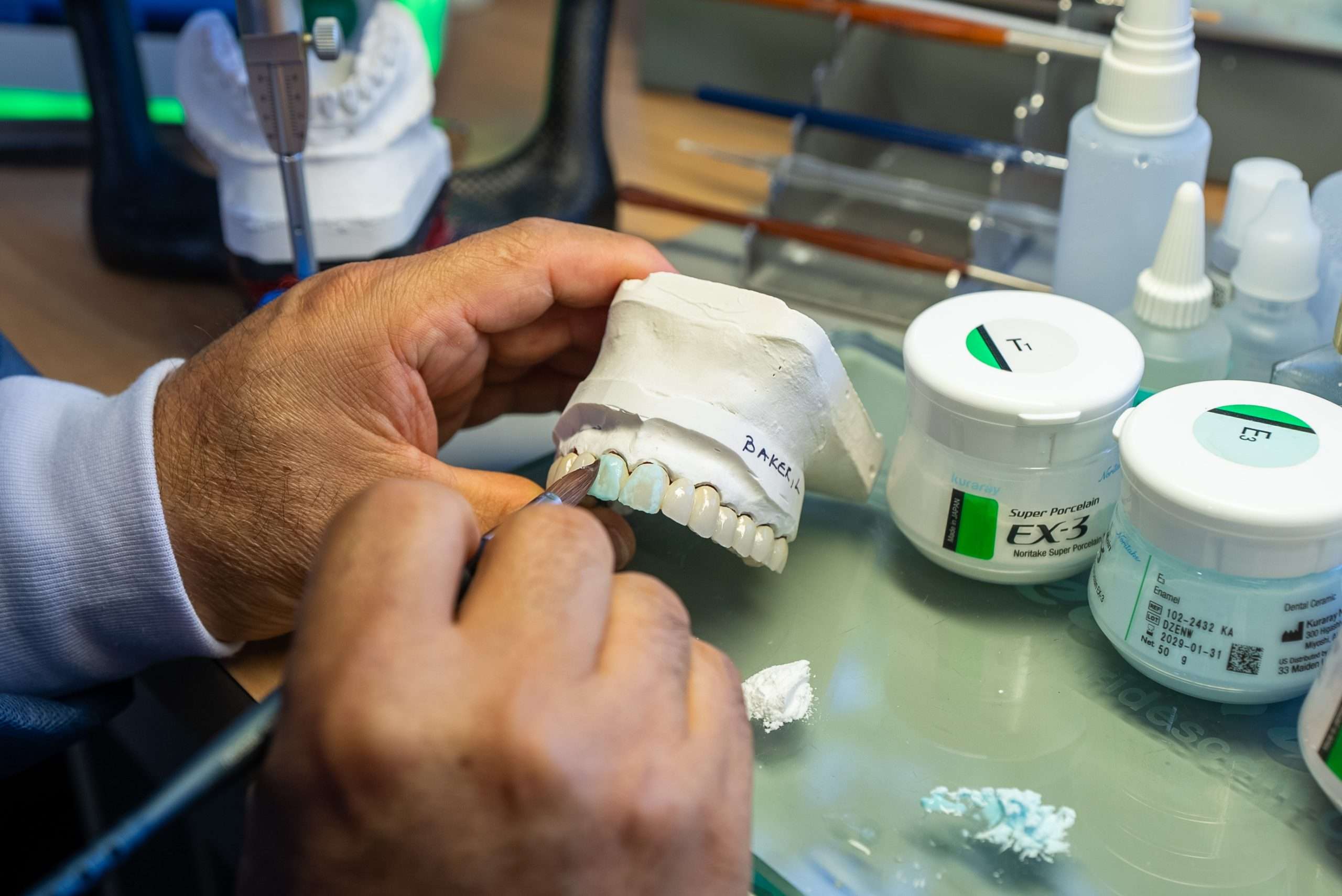 A person uses a tool to adjust a dental model with artificial teeth on a desk in Bethesda, surrounded by dental implants materials and containers.
